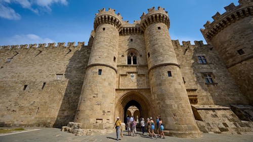Super wide angle shot, several people admiring a mighty castle with watchtowers and blue sky in the