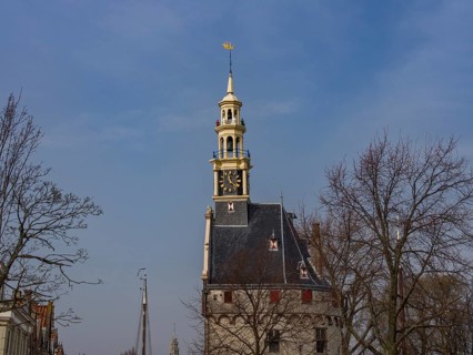 Historic clock tower with trees and blue sky in the background, tower with a golden spire and a