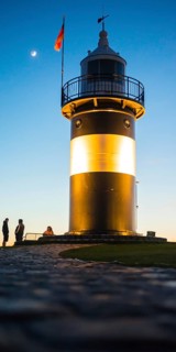 Black and white lighthouse, called 'Kleiner Preusse', stands illuminated at night shortly after