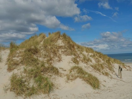 High sand dunes with grass, above a sky with some clouds, dunes on an island with a blue boat and a