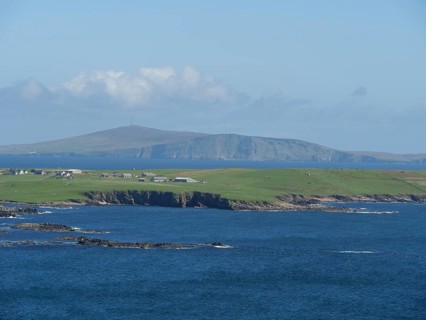 View of the tranquil coastal landscape with houses and hills in the background, green meadows by a