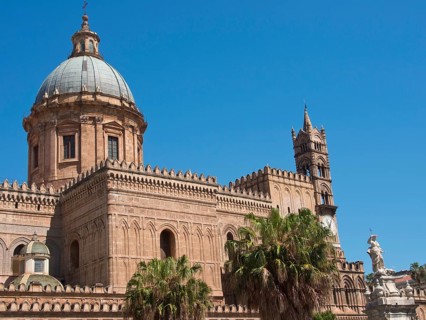 Historic cathedral with large dome and small town character, surrounded by palm trees, under a blue