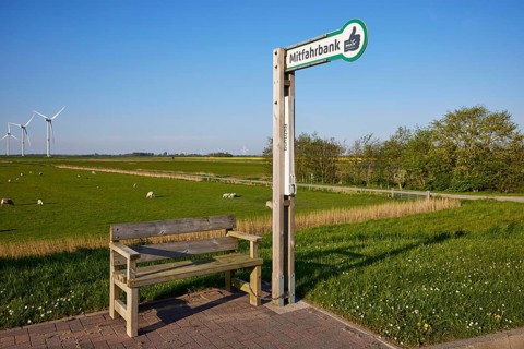 Carpooling bench in the marsh landscape with sheep and wind turbines near Simonsberg, Nordfriesland