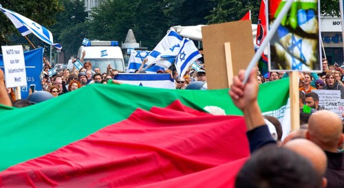 Protesters of the Al Quds demonstration with a large Palestinian flag march past the pro-Israel