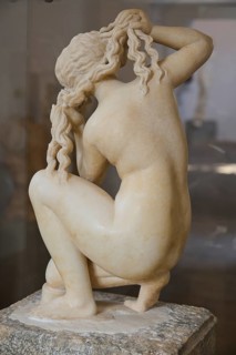 Aphrodite, crouching, rear view of a kneeling female sculpture braiding her hair, graceful and