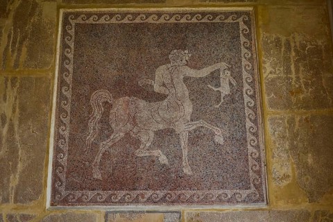 Antique mosaic with a centaur holding a rabbit, surrounded by decorative patterns, outdoor area,