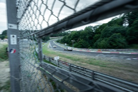 Cars race past on a race track, seen through a safety fence. Nuerburgring race track, Nuerburg