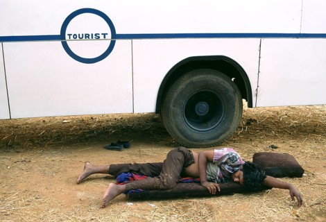 Attendant sleeping near the bus where he is employed, teenage boy working in poor conditions work,