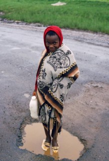 Girl washing her shoes in a puddle, rainy day in Lesotho, girl from the Basotho ethnic group,