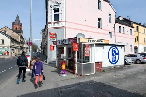 A pedestrian walks past a kiosk in Gelsenkirchen with a large S04 logo of FC Schalke 04 on it,