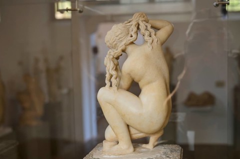 Aphrodite, crouching, rear view, sculpture of a naked woman tying her hair in a classical style in
