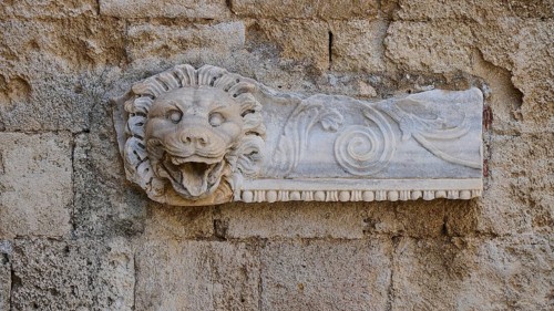 Ancient stone relief of a lion's head, carved into a wall, rich in details and textures, outdoor