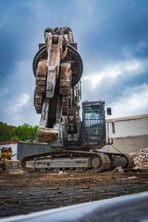 An excavator with a grab arm sits on a construction site with demolished buildings and bricks,