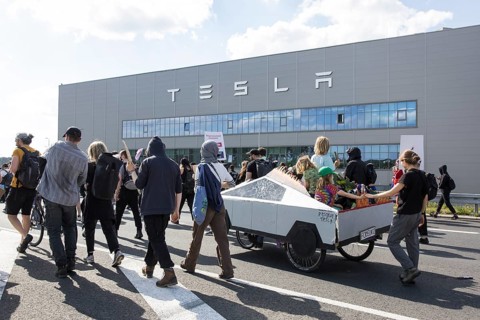 Participants with a Cybertruck cardboard model on a bicycle in front of the Tesla Gigafactory