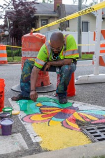 Detroit, Michigan, Artist Trae Isaac paints a design on a city street. He is part of City Walls, a