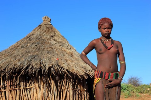 South Ethiopia, Omo region, young woman of the Hammer people standing in front of a round hut,