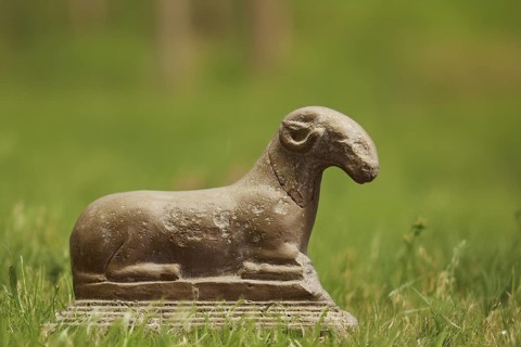 Ceramic sculpture of a ram, motif cropped, meadow background KI generated, Antique stone sculpture