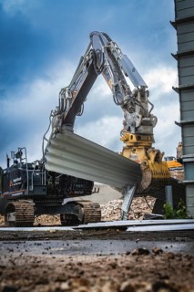 A large excavator lifts building materials on a construction site, the sky is cloudy and the