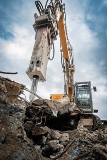 An excavator on a construction site working on a pile of rubble, large pieces of metal next to it,