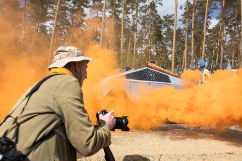 A Tesla Cybertruck made of cardboard between the smoke of an orange fog pot during the