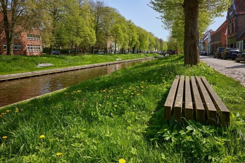Public wooden bench between trees on the banks of the Mittelburggraben in Friedrichstadt,