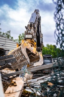 An excavator's metal tongs move rubble and debris in a construction site with green background,