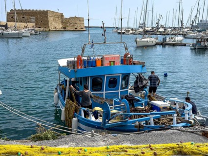 In the foreground yellow fishing net from behind local Greek fishermen arranging their nets on