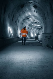 A person in a safety waistcoat walks through an illuminated, dark tunnel with a futuristic