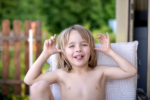 Boy, 5 years, blonde, sitting in garden chair, garden, grimacing, sticking out tongue, summer,