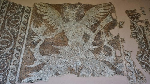 Antique mosaic of a winged creature, sea god Triton, damaged, shows detailed mythological