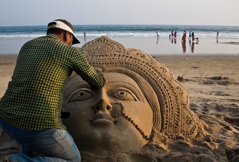 Sand artist sculpting a sand sculpture, sculpture representing the hindu goddess Lakshmi, beach at