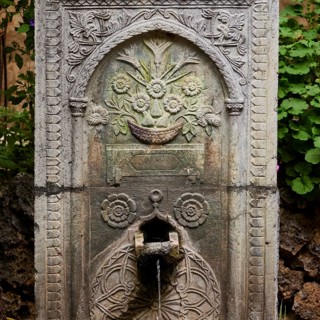 Artfully engraved stone fountain with plant motifs, water flowing out, outdoor area, Archaeological
