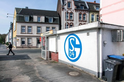 A pedestrian walks past a kiosk in Gelsenkirchen with a large S04 logo of FC Schalke 04 on it,