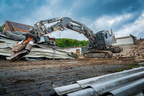 A heavy excavator lifts materials on a construction site full of rubble and pieces of metal, grey