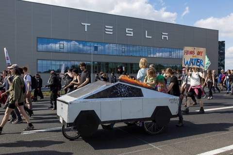 Participants with a Cybertruck cardboard model on a bicycle and sign Hands off our water in front
