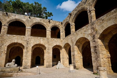 Courtyard of a medieval fortress under a blue sky, surrounded by trees with lion statue, outdoor