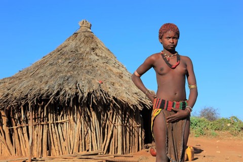 South Ethiopia, Omo region, young woman of the Hammer people standing in front of a round hut,