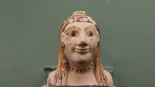 Aryballos, ceramic vessel, ancient bust of a face against a green background, partially damaged,