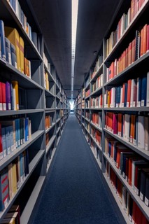 A narrow corridor between high bookshelves in a library with multi-coloured books that radiate a