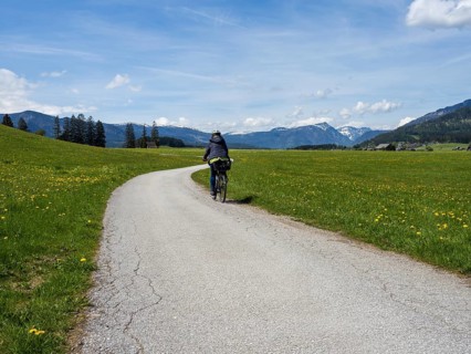 Path leads through green meadows, cyclist on the Salzkammergut cycle path, cloudy mood over