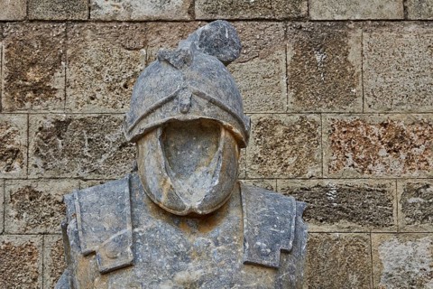 Stone figure of a headless knight in armour in front of a rustic wall, outdoor area, Archaeological