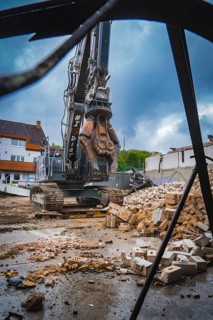 An excavator stands on a construction site, surrounded by rubble and bricks, under a cloudy sky,