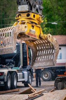 Yellow excavator arm with grapple on a construction site, wood chips and lorry in the background,