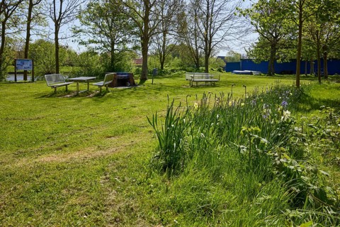 Small park with flowers, lawn and a public barbecue area with brick barbecue, benches and tables in