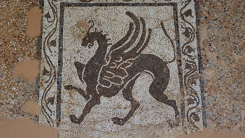 Antique mosaic with a winged mythological horse surrounded by decorative patterns, outdoor area,
