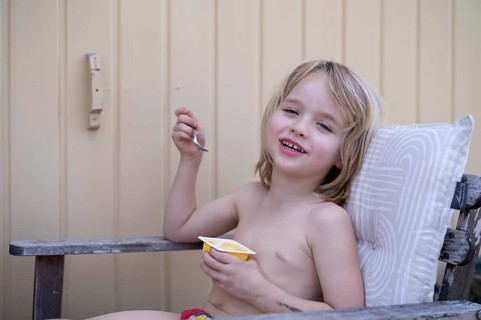 Boy, 5 years, blonde, sitting in garden chair, garden, eating pudding, yoghurt, enjoying, summer,