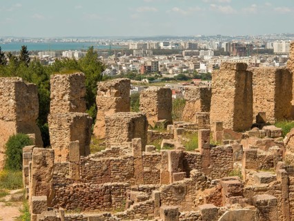 Historic stone ruins with a view of the modern city in the background, sweeping views under a blue
