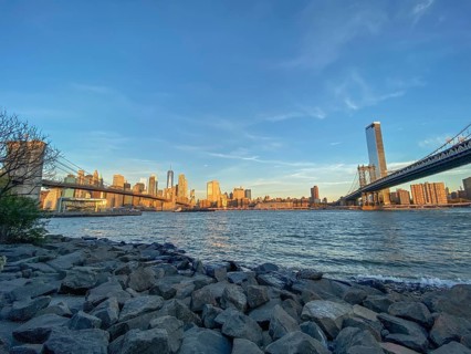 Manhattan skyline with bridges over the river at sunset seen from the shore, historic bridge in the