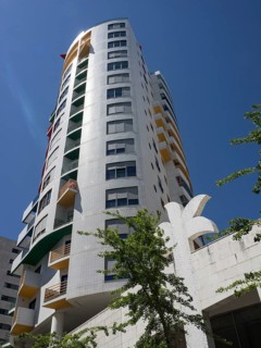 A modern high-rise building with balconies and colourful elements under a clear blue sky, Lisbon,
