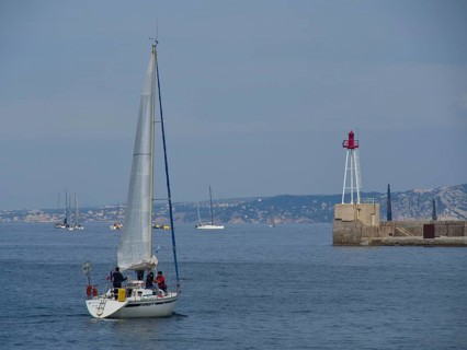 Sailing boat on the open sea, in the background more boats and a lighthouse, Marseille on the
